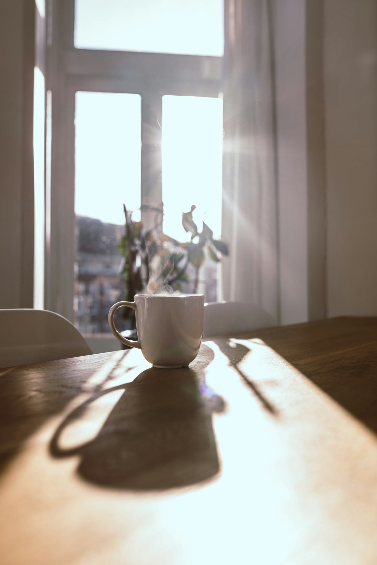 Photo d’illustration : une tasse fumante sur une table en bois, dans le soleil du matin.